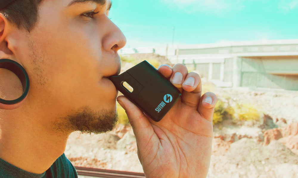 Man vaping with Sutra Mini in front of beach house under bright natural lighting