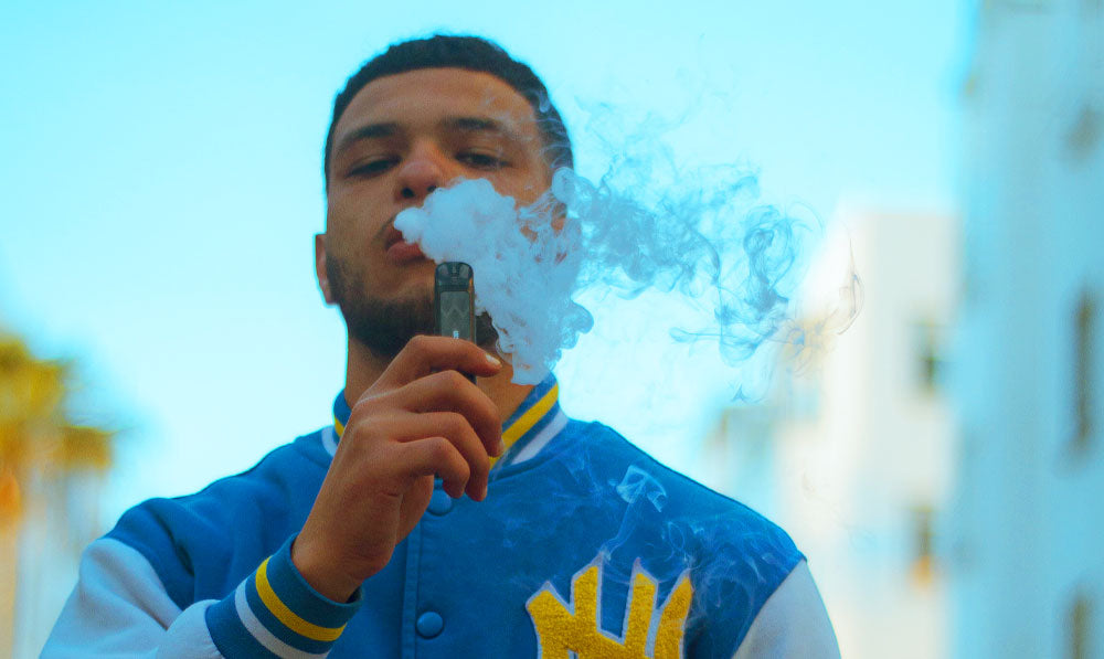 Man in letterman jacket vaping outside with natural lighting