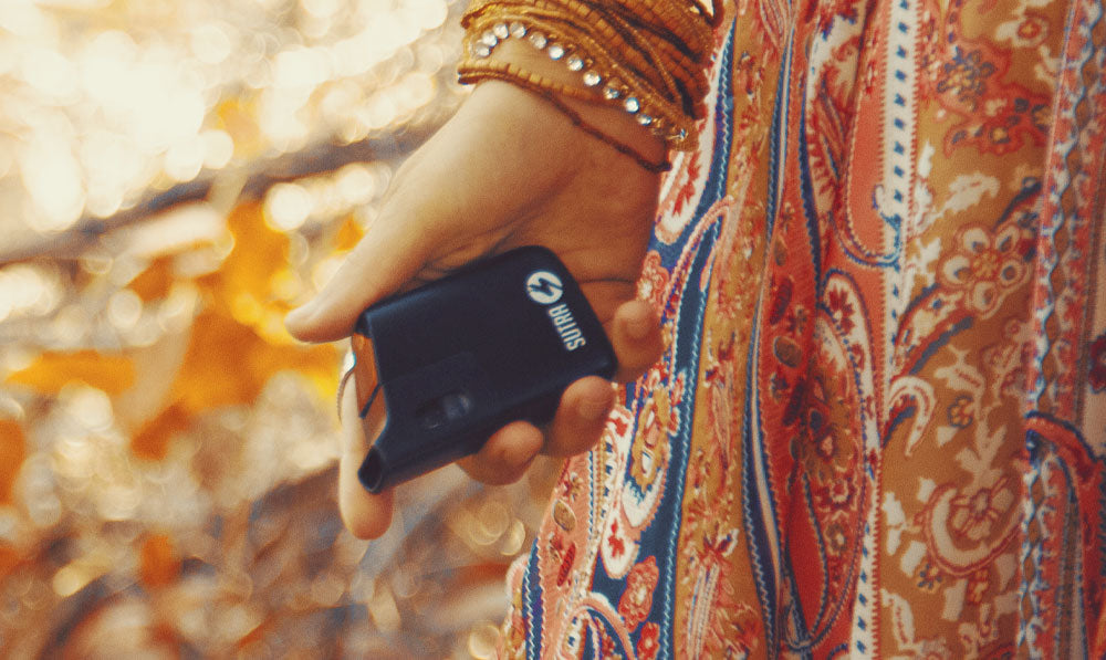 Woman holding Sutra Mini by her side during fall with autumn leaves behind