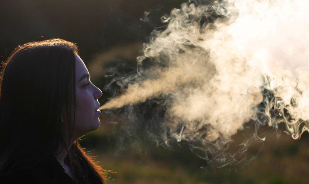 Woman blowing vape smoke at a park