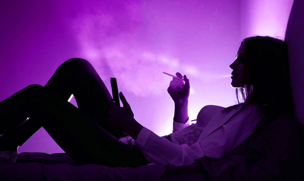 Woman laying down relaxing and vaping with soft purple studio lighting