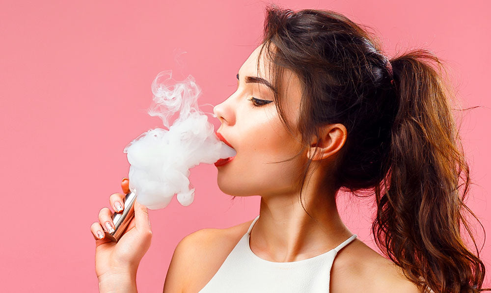 Pretty woman vaping in front of pink studio background