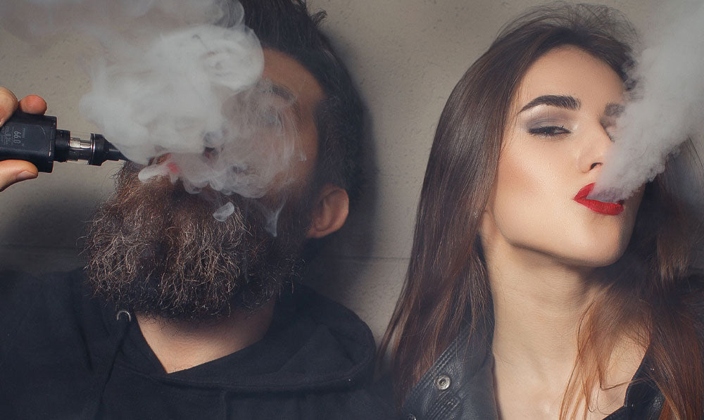 Two vapers puffing outwards in front of a wall