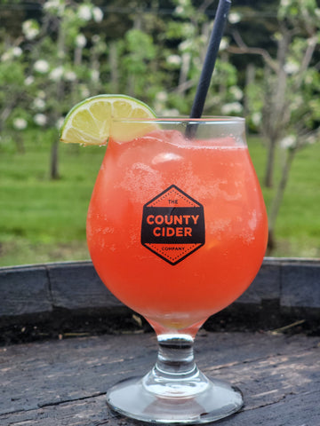 A photo of a cosmo cocktail in a glass with a straw in it and a lime