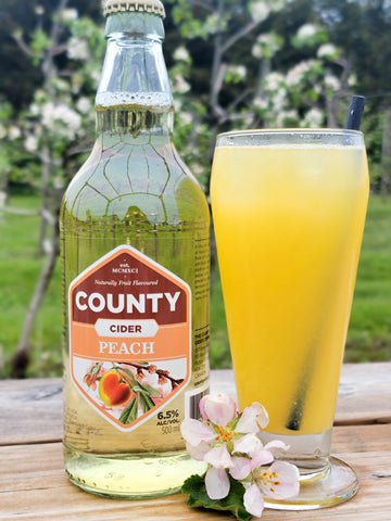 A photo of a bottle of peach cider next to a cocktail glass