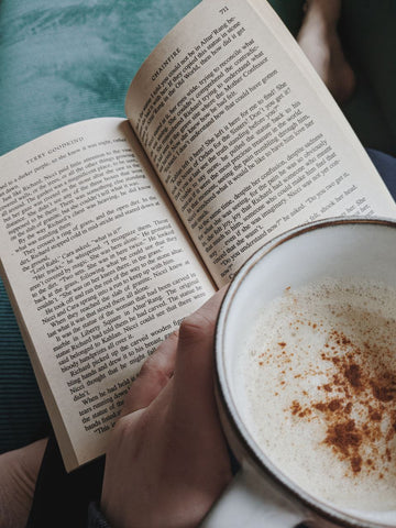 Hands holding a book and a cup of coffee with cinnamon