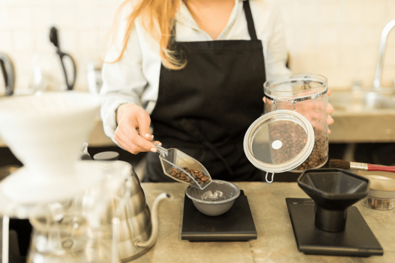 Barista measuring out coffee beans with a scoop and putting them on a scale