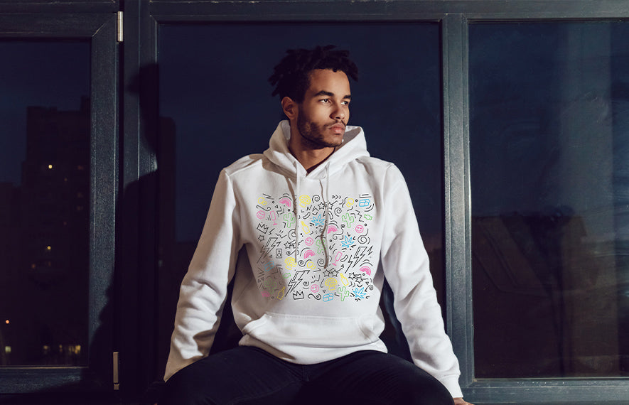 Male wearing white indulge neon scribbles hoodie sitting in front of window.