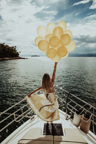 woman standing at the tip of a boat deck with balloons in her hand