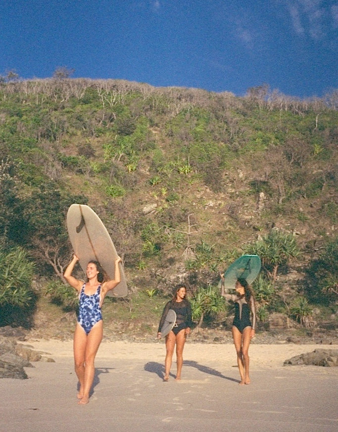 three girls walking with surfboards