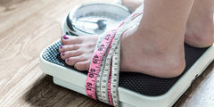 Feet strapped to some weighing scales by measurement tape, representing our attachment to weight and body image