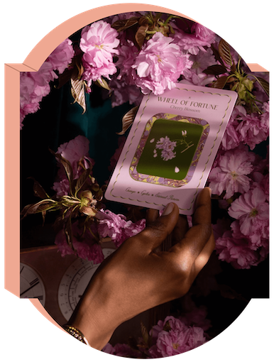 An elegant hand plucks The Garden Journey Deck's Wheel of Fortune card from cherry blossoms