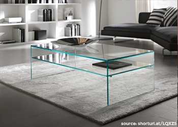 A photo of a clear glass surface, reflecting light and objects in the surrounding environment. The glass appears to be flat and smooth, with no visible scratches or blemishes. The photo may show a piece of glass used as a tabletop or surface in furniture, such as a coffee table or desk. 