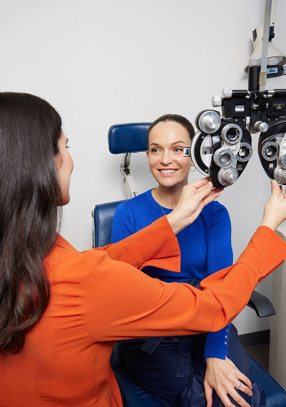 Optometrist adjusting phoropter during eye examination with female patient.
