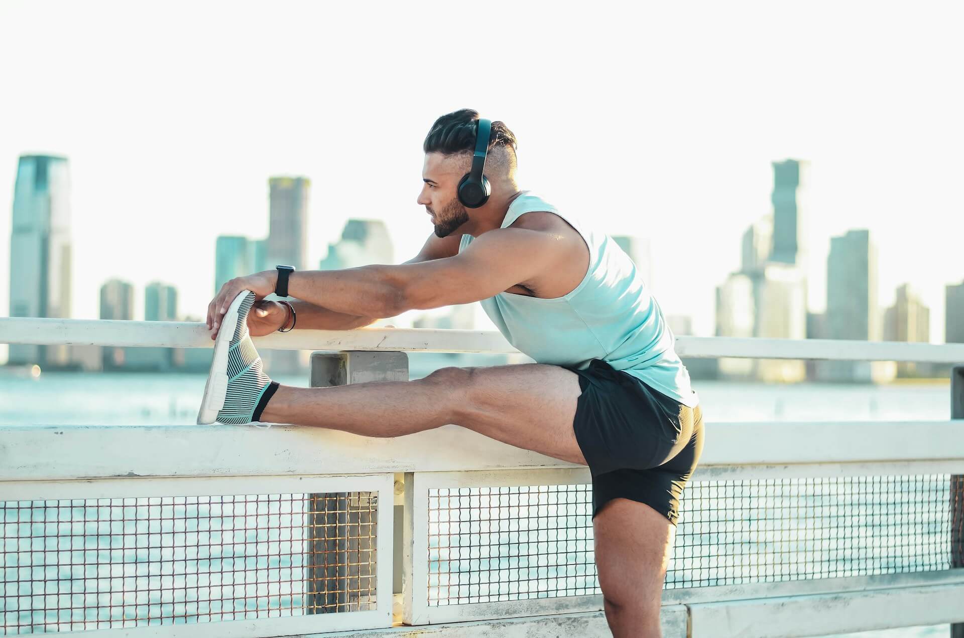 Man doing a leg stretch over the fence with the city in the background