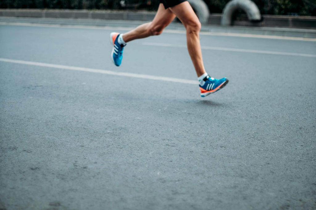A runner with athletic toe socks and blue shoes sprints down the road