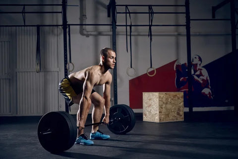 A man in black shorts at the gym in the start position for a barbell deadlift.