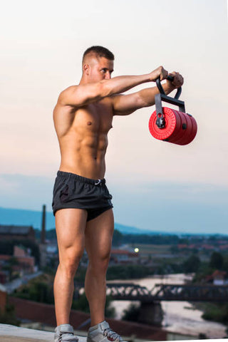 Muscular man in black shorts holding a weight out in front of him with arms extended. 