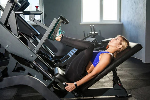 Woman wearing black leggings and a sport top seated at the leg press machine with her feet in the start position.