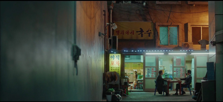 Two men eating outside in an alley at night