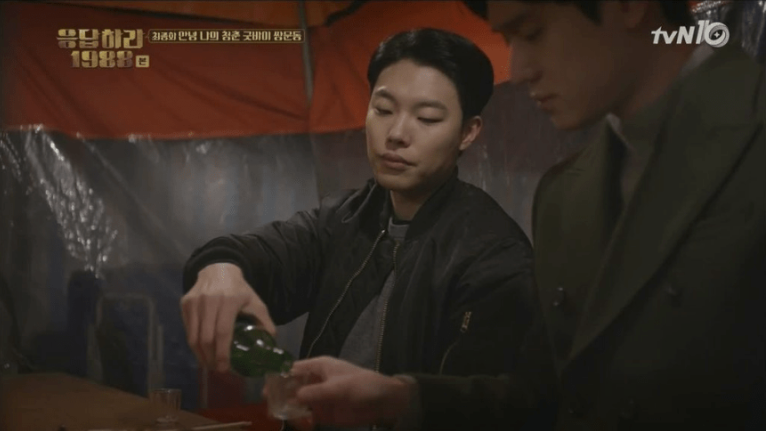 A man pouring a guy more soju in a food tent