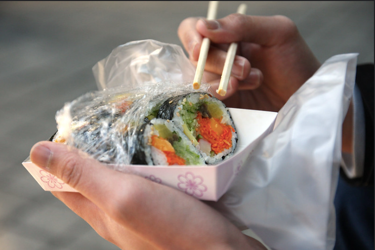 A person holding a pink lunch box with gimbap and chopsticks