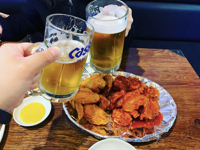Two people clinking glasses of beer over fried chicken