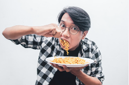 An Asian man eating instant noodles with the fork in his mouth