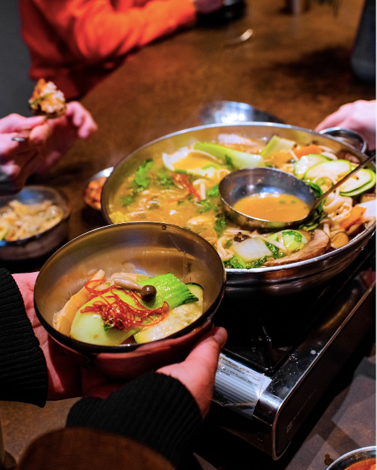 A person holding out a bowl of Korean hot pot