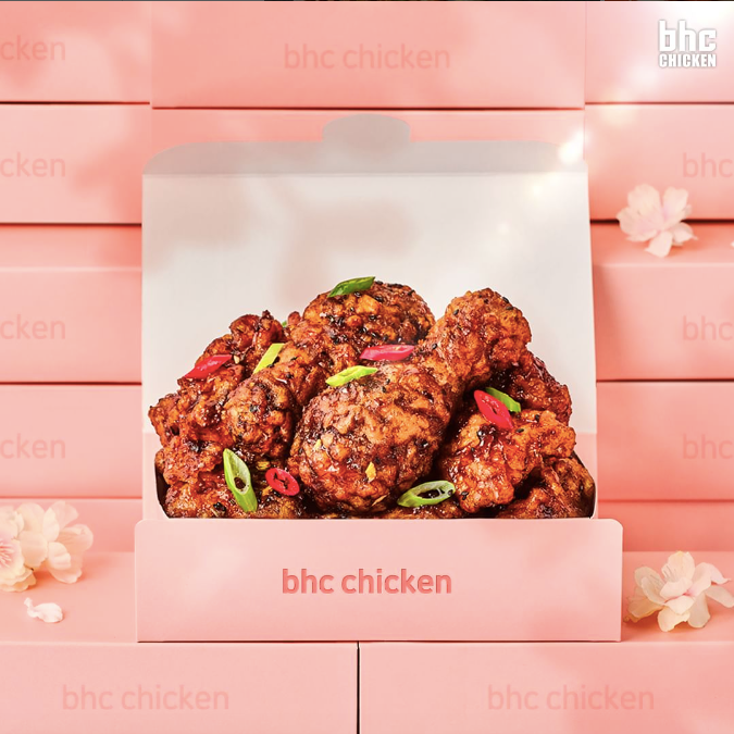 Fried chicken in a pink takeout box on a pink bench with flowers and BHC logo