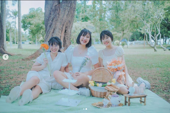 Three girls in white picnic dresses with a picnic set under a tree