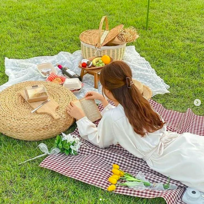 A girl wearing a white dress with long sleeves reading a book on a picnic blanket