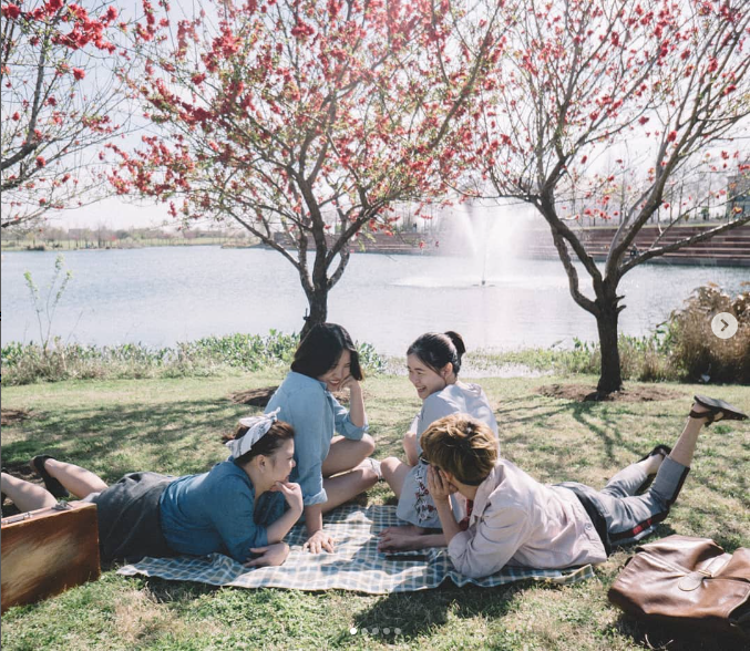 Three girls and a boy wearing pants/denim in front of a river at a picnic
