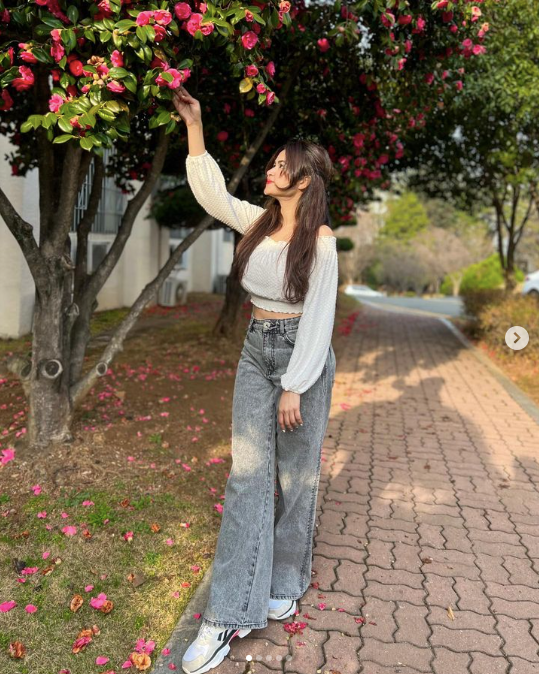 A girl wearing a long cotton top and wide-ankle jeans under a tree