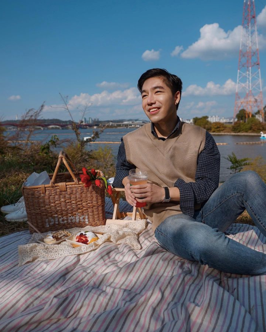 A man wearing a brown vest over a blue top holding a glass at a picnic