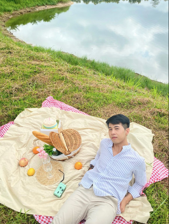 A man wearing a button-up shirt on a picnic blanket by a lake