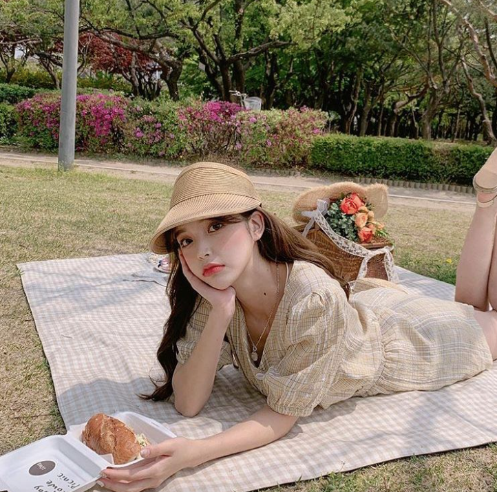 A girl wearing a hat and cute dress on a picnic blanket