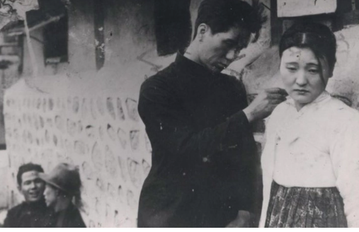 A man touching woman's shoulder while two men sit against a wall