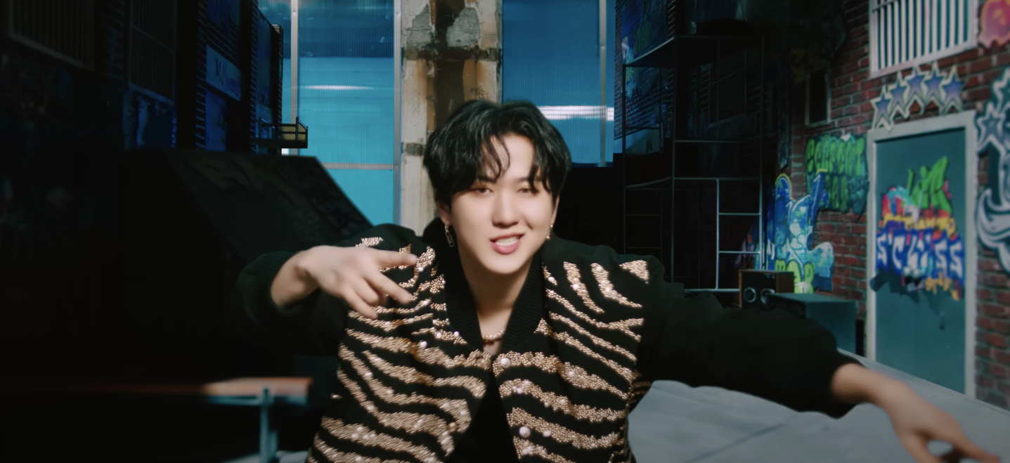 Changbin smirking at the camera in a graffiti-lined alley