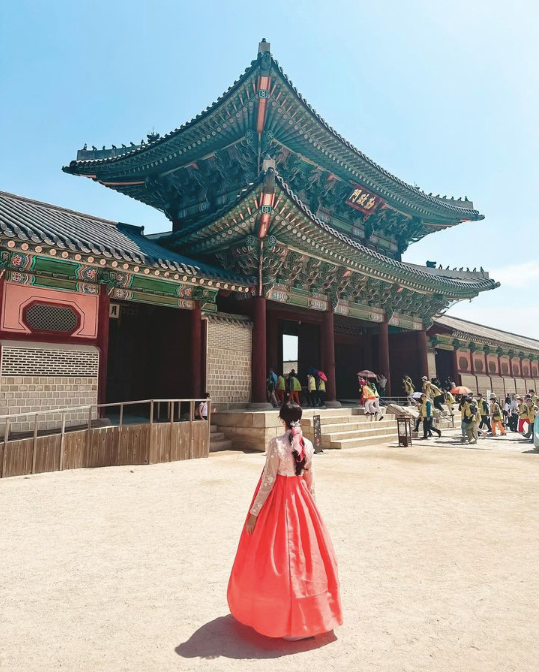 A woman wearing peach and pink hanbok in front of Gyeongbokgung Palace