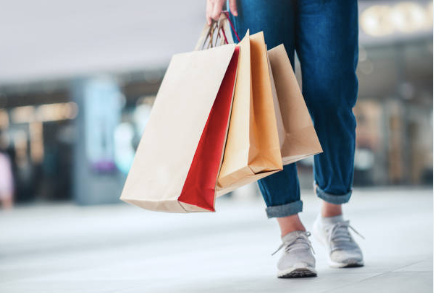 Person wearing jeans and white sneakers holding paper shopping bags