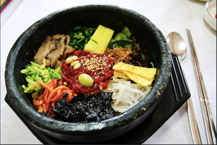 Bibimbap in a stone bowl with metal chopsticks and spoon on the side