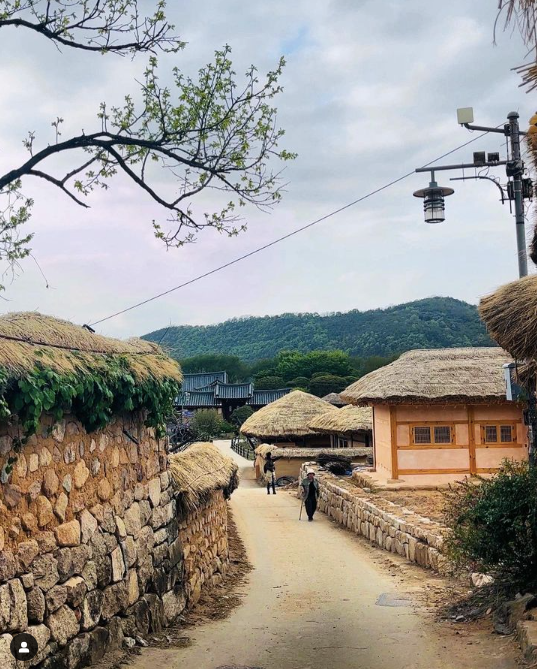 A woman in black walking down a stone wall-lined lane with traditional Korean houses