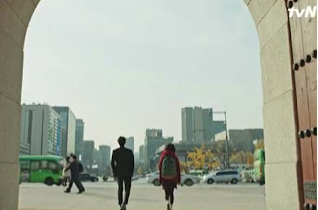 A man in a suit and a girl wearing a red scarf and skirt walking away from camera