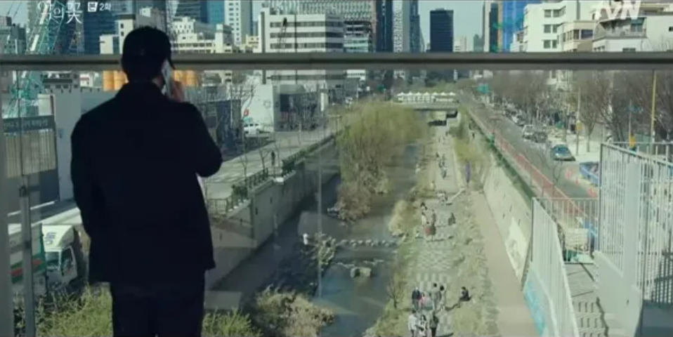 A man's back to the camera on the phone looking at Cheonggyecheon from bridge