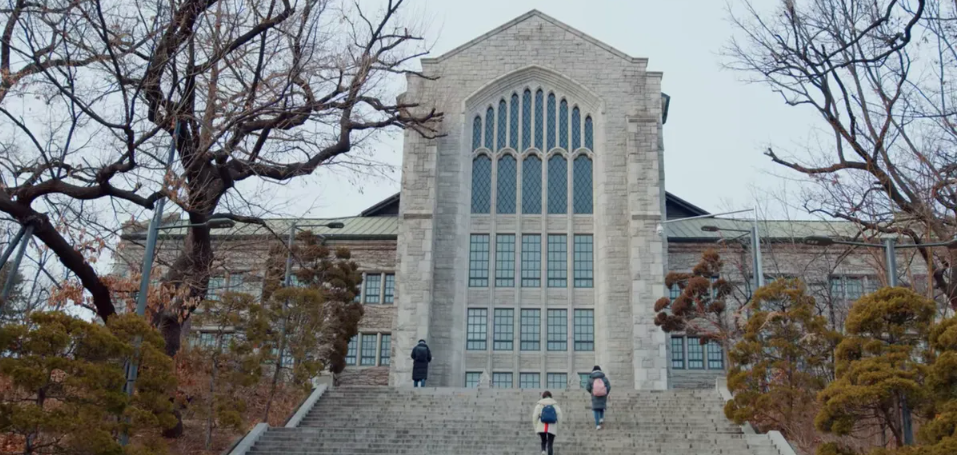 A stone arrow-shaped building with blue windows and stairs with people climbing them