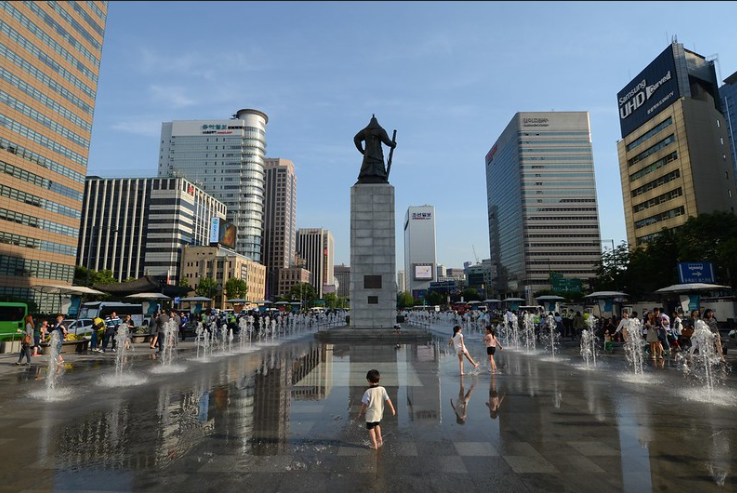 A child playing in the wet Gwanghwamun Square in front of Admiral Yi statue
