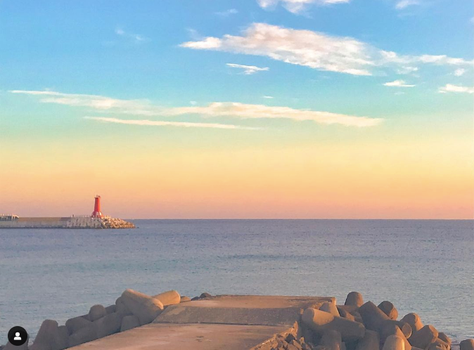 A cement port at sunset with red lighthouse in the distance