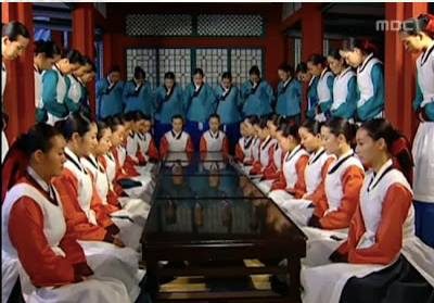Rows of female doctors in red and white facing each other and kneeling with soldiers in blue behind them