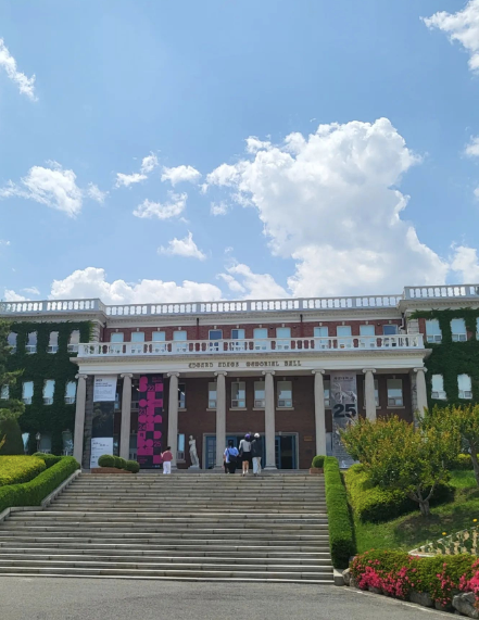 A white columned red building with stone steps and green bushes